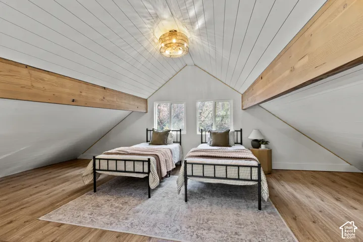 Vaulted ceiling with exposed wood beams, wood-finish flooring, and white paneled walls