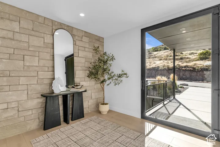 Stone accent wall, wood-finish flooring, recessed ceiling lighting, large glass door, and exterior balcony with metal railing