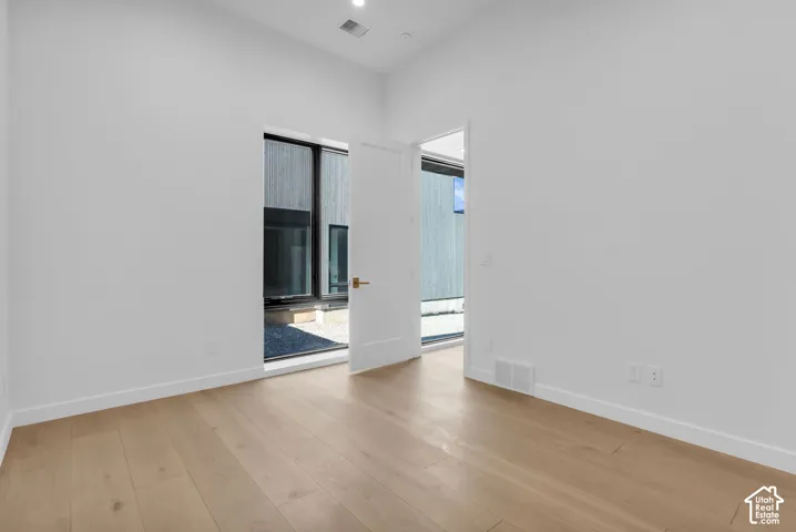 Light wood-finish flooring, recessed ceiling lighting, a white painted door with brass hardware, and a window with dark framing