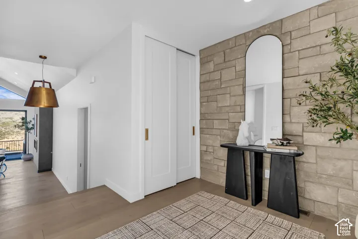 Stone accent wall, wood-finish flooring, vaulted ceiling, brass pendant light fixture, and white sliding doors