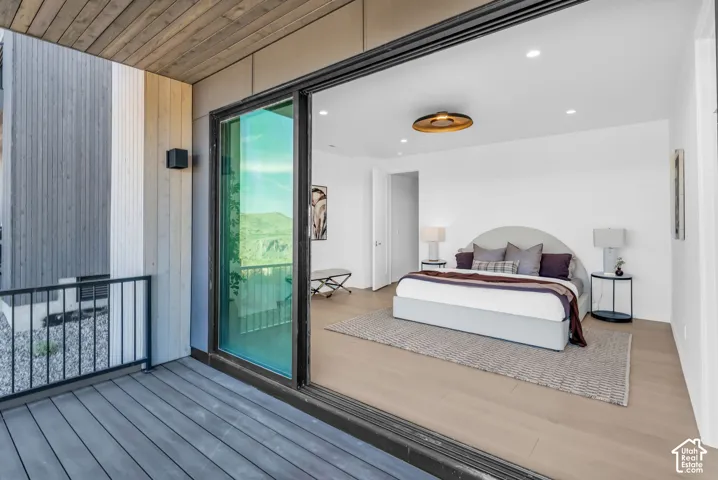 Expansive private balcony with composite decking and black metal railing, offering direct access to a room with wood-finish flooring, recessed lighting, and a contemporary ceiling fixture