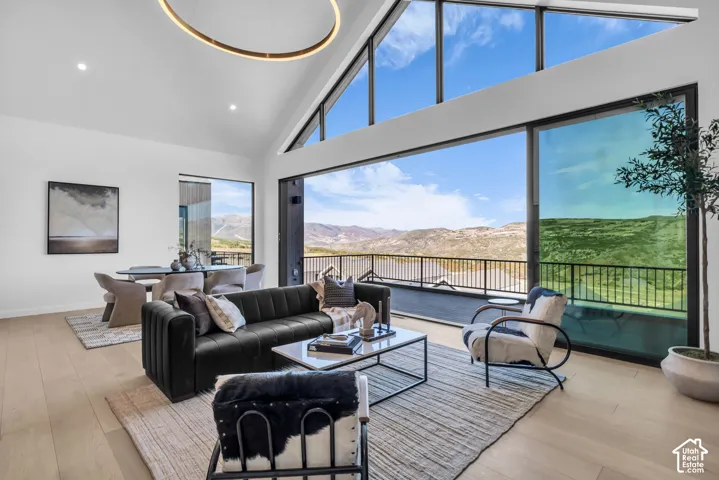 Vaulted ceiling with recessed lighting, expansive glass sliding doors, integrated dining area, wood-finish flooring, and a large outdoor balcony with a metal railing