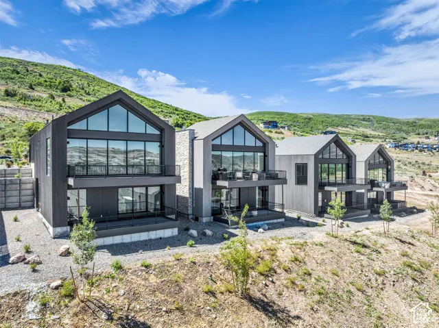 Modern architectural design featuring expansive glass panels, multiple private balconies with metal railings, and a distinct gabled roofline