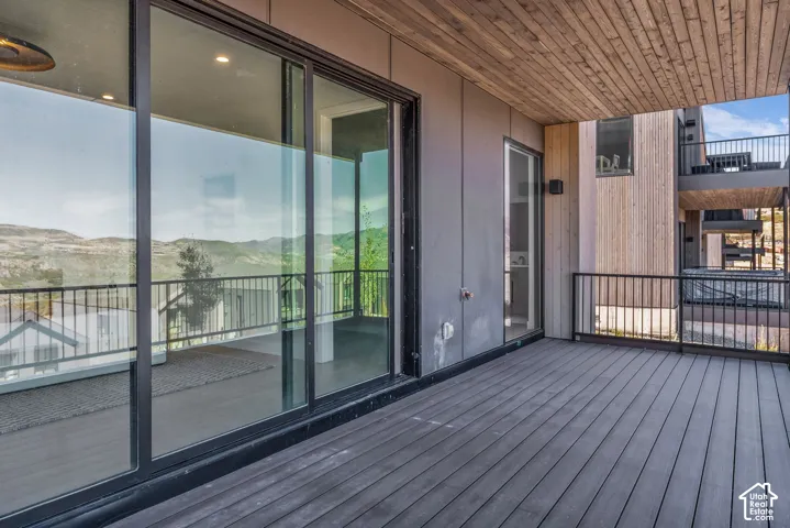 Expansive exterior deck with wood-finish flooring, black metal railing, and large sliding glass doors