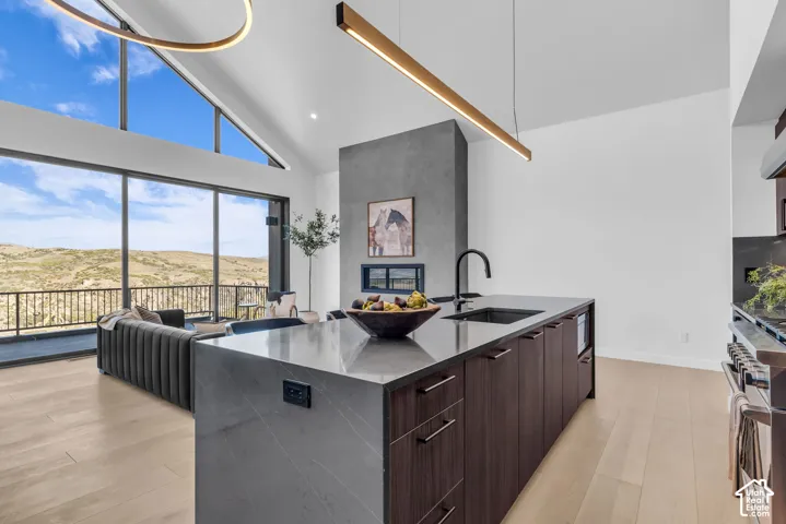 Vaulted ceiling with linear lighting, expansive window wall, contemporary fireplace, island with integrated sink, and wood-finish flooring