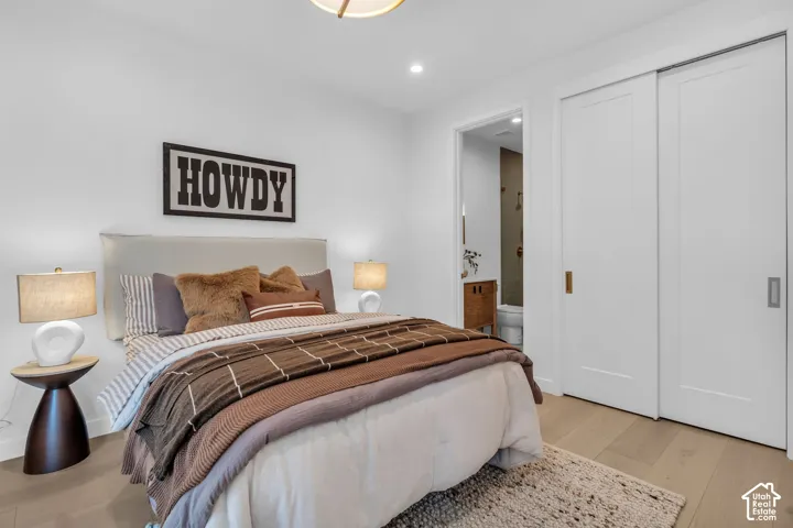 Recessed lighting, wood-finish flooring, white walls, built-in sliding closet doors, and an attached bathroom with a vanity
