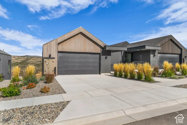 Modern exterior featuring a prominent garage, a covered entry, wood siding accents, and a concrete driveway