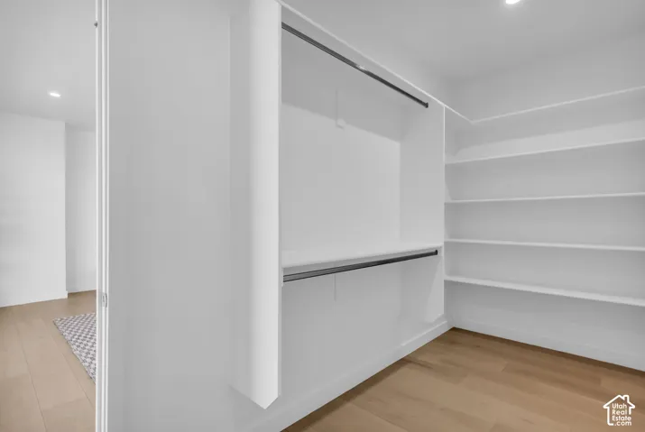 Expansive closet featuring integrated shelving, two clothing rods, and wood-finish flooring