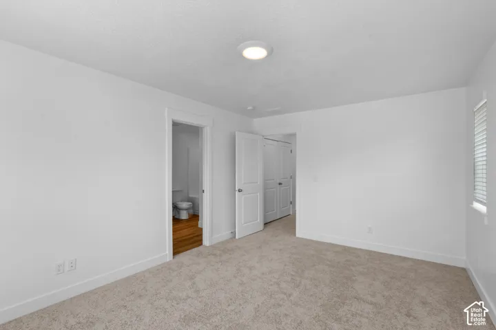 Neutral tone wall finish, wall-to-wall carpeting, recessed ceiling light fixture, white interior doors, and a window with blinds