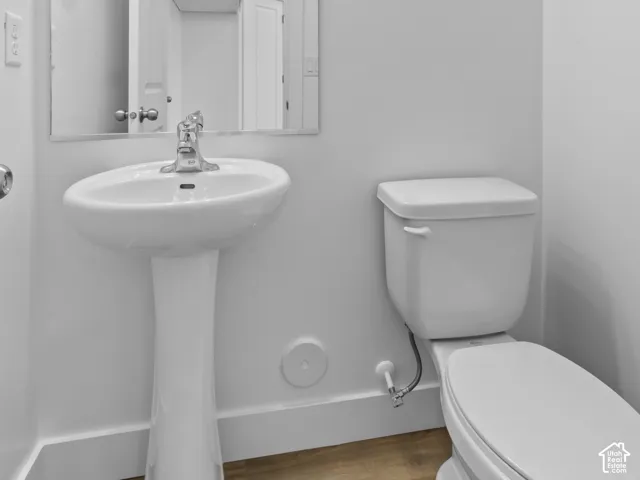 Pedestal sink with chrome faucet, wall-mounted mirror, and wood-finish flooring