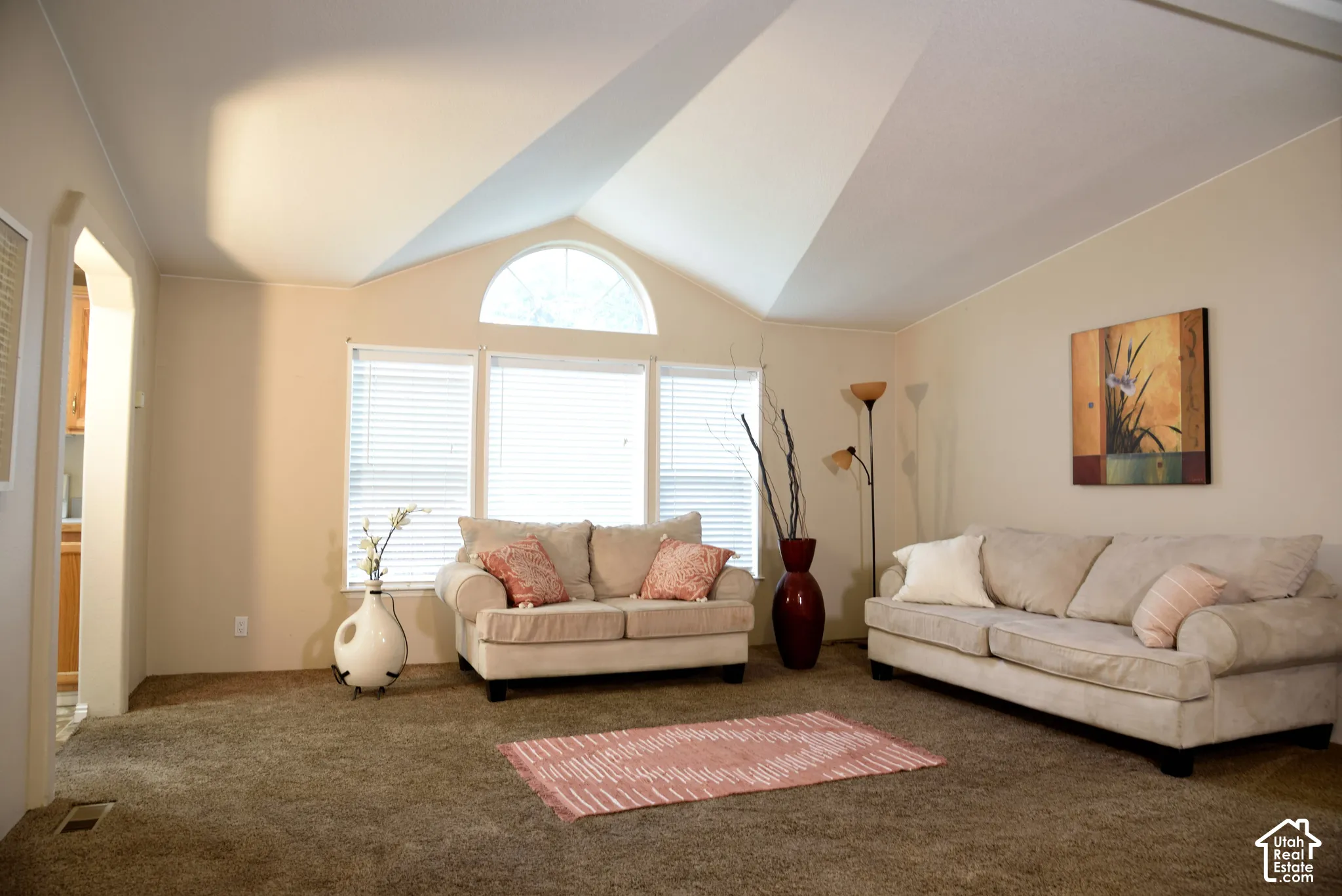 Vaulted ceiling, arched transom window, large window array, neutral wall tones, and carpeted flooring