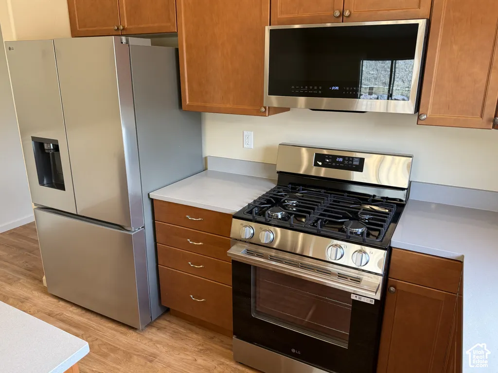 Stainless steel refrigerator, range, and microwave with wood-finish cabinetry and light-toned countertops