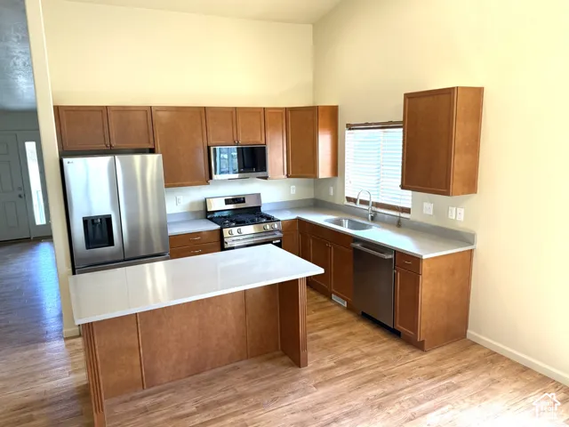 Kitchen featuring wood-finish flooring, light-toned countertops, wood cabinetry, stainless steel appliances, and a built-in sink