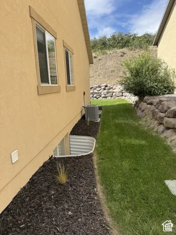 Stucco exterior with multiple windows, landscaping with dark wood mulch, and a foundation-level window well