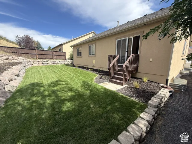 Expansive backyard featuring a manicured lawn, stone retaining walls, privacy fencing, a ground-level deck, and sliding glass door access