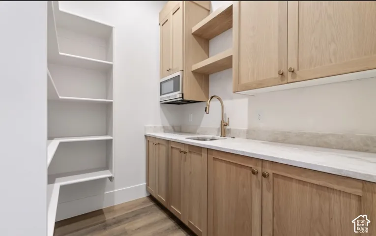 Light wood-finish cabinetry with brass hardware, undermount sink with gooseneck faucet, light-toned countertop, and built-in microwave