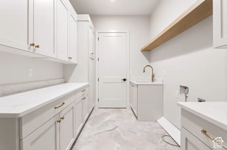 White shaker-style cabinetry with gold-finish hardware, light-toned countertop, integrated sink with gold-finish faucet, and a wood-finish floating shelf