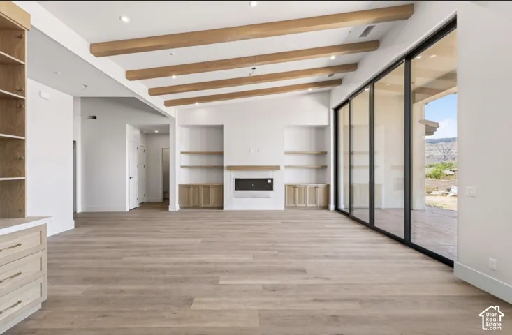 Vaulted ceiling with exposed wood beams, wood-finish flooring, built-in shelving, integrated fireplace, and large sliding glass doors