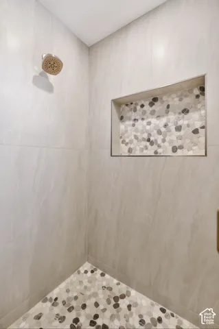 Tiled shower enclosure featuring a built-in niche with pebble mosaic, a rain shower head, and a matching pebble-finish shower floor