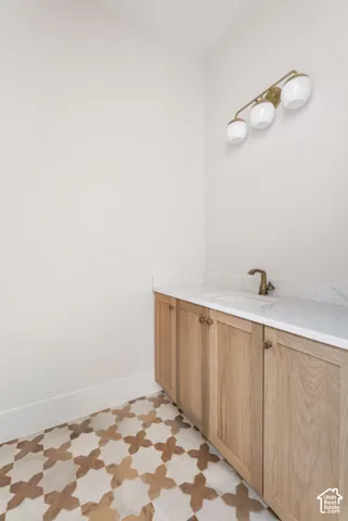 Custom patterned floor tile, light wood-finish cabinetry, white countertop, integrated sink, and bronze-finish faucet