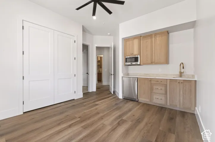 Wood-finish flooring, built-in cabinetry with stainless steel appliances, modern ceiling fan, and white panel doors