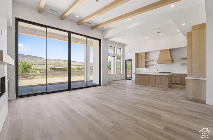 Expansive sliding glass doors, wood-finish flooring, exposed ceiling beams, recessed lighting, and a kitchen island with built-in cabinetry