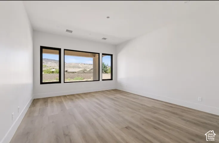 Expansive room featuring wood-finish flooring, white walls, and a large window array with black frames