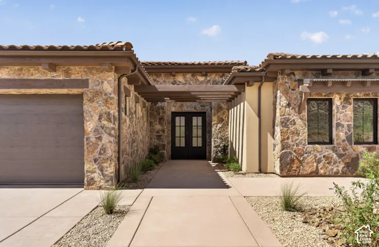 Exterior featuring stone cladding, a tiled roof, an integrated garage, a double entry door with glass panels, and a decorative pergola element