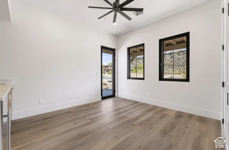 Wood-finish flooring, white walls, black-framed windows, ceiling fan with integrated lighting, and a glass-paneled exterior door