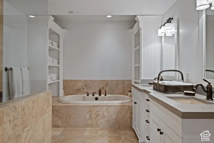 Built-in soaking tub with stone surround, dual vanity with undermount sinks, and integrated shelving