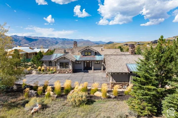 Contemporary residence featuring a multi-gabled roofline with shake and metal roofing, a stone and siding exterior, an expansive paved driveway, and mature landscaping