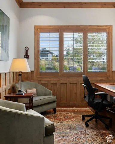 Wood-paneled walls and ceiling beams, three-panel window with shutters, desk with wood-finish top
