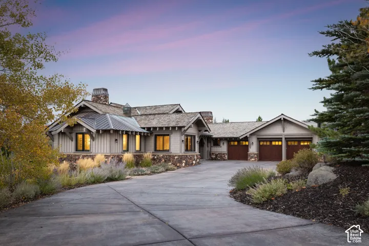 Craftsman-style architecture featuring stone and wood siding, a multi-paneled garage door, a prominent stone chimney, and a concrete driveway