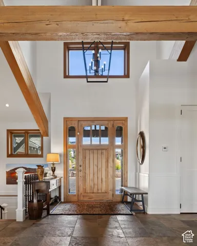 Vaulted entry with exposed wood beams, slate tile flooring, a solid wood front door with sidelights, and a black wrought iron chandelier