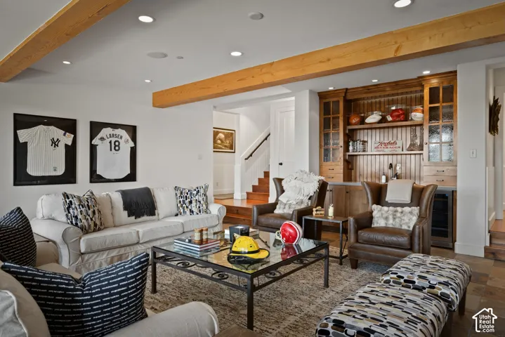 Exposed wood ceiling beams, recessed lighting, built-in cabinetry with glass-front uppers, wood-finish flooring, and a staircase with a dark handrail