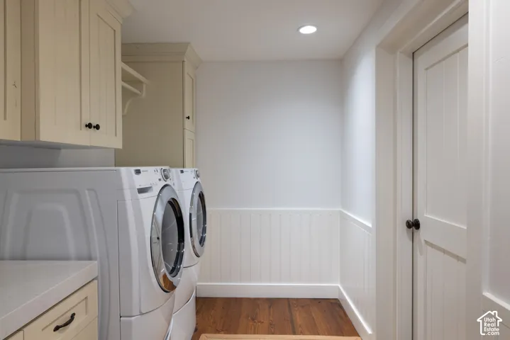 Laundry area featuring wood-finish flooring, beadboard wainscoting, cream cabinetry with black hardware, and an integrated countertop