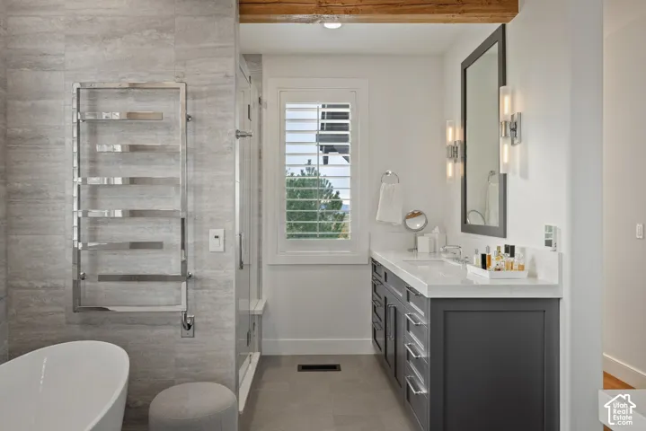 Freestanding soaking tub, polished chrome towel warmer, glass-enclosed shower, dual-sink vanity with under-counter storage, and exposed wood beam