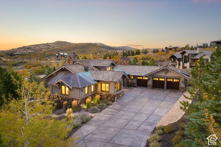 Stone and wood siding exterior with a multi-car garage, concrete driveway, and natural landscaping
