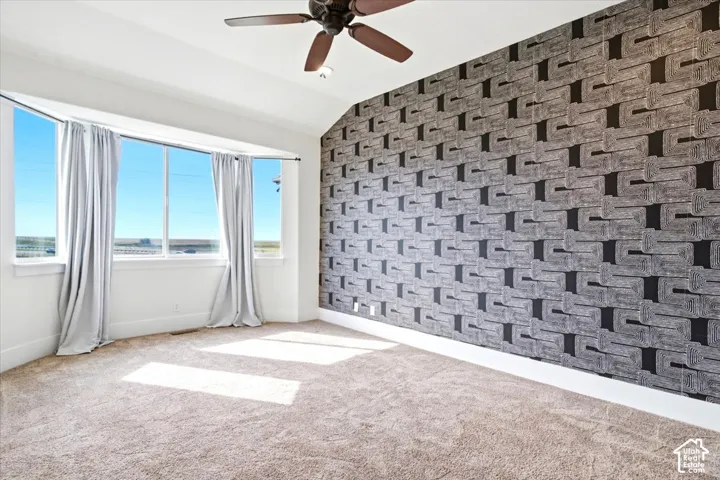 Bay window with multiple panes, textured accent wall, ceiling fan, vaulted ceiling, and neutral-toned carpet