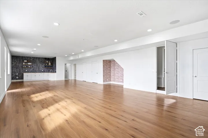 Expansive open-concept room featuring wood-finish flooring, recessed lighting, and built-in cabinetry with a dark-toned backsplash