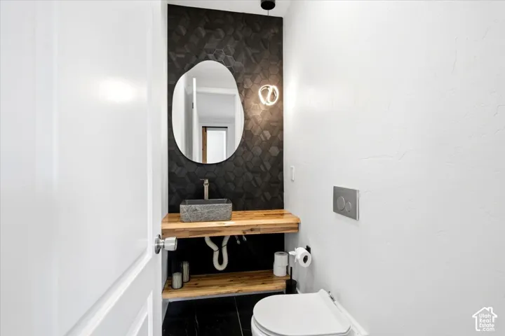 Modern powder room featuring a stone vessel sink, wood-finish floating vanity, geometric black tile accent wall, and a contemporary wall-mounted light fixture