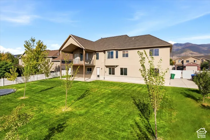 Expansive green lawn, two-story residence with a covered upper balcony, and a lower patio area