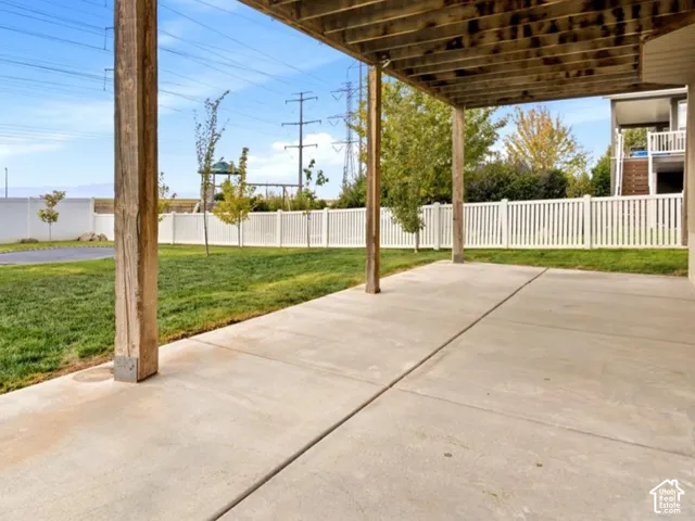 Covered concrete patio with a spacious lawn and white privacy fencing