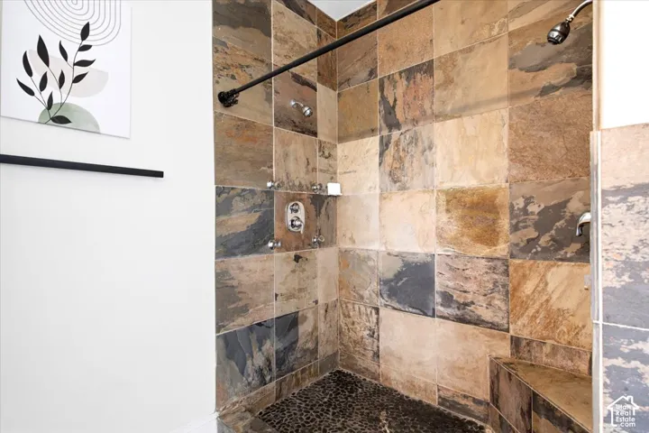 Spacious shower with large format natural stone tile, pebble floor, built-in bench, and black-finish fixtures
