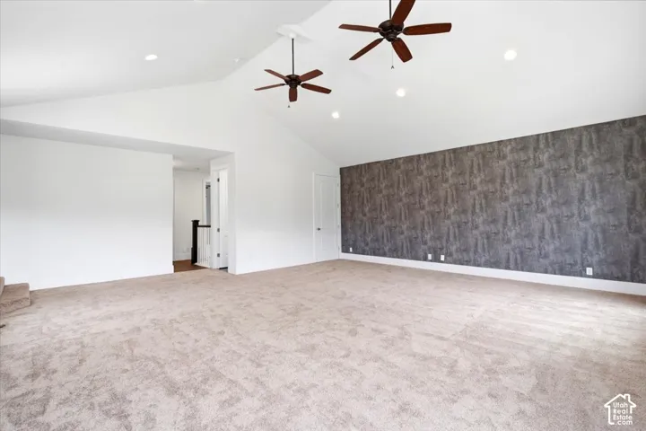 Vaulted ceiling with recessed lighting, two ceiling fans, textured accent wall, and neutral carpeting