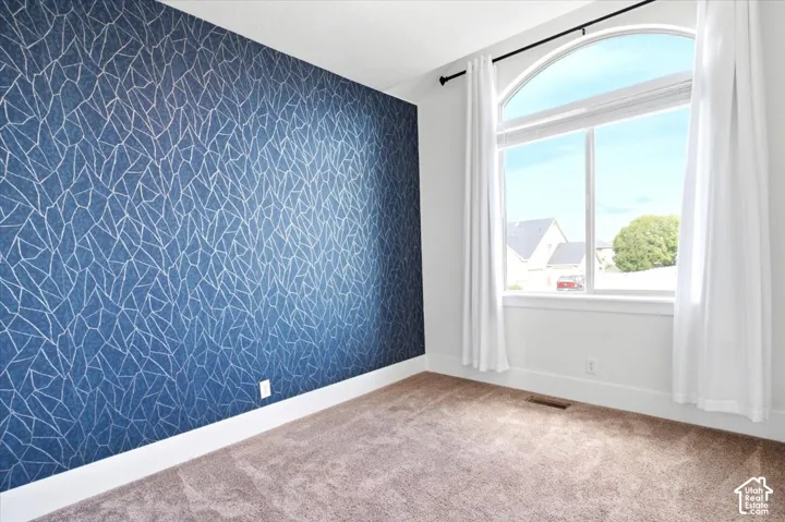 Arched window with white trim, blue patterned accent wall, and tan carpeting