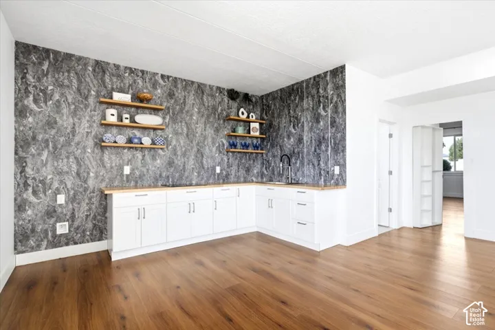 Wood-finish flooring, white cabinetry, light-toned countertops, a black sink faucet, and floating wood shelves