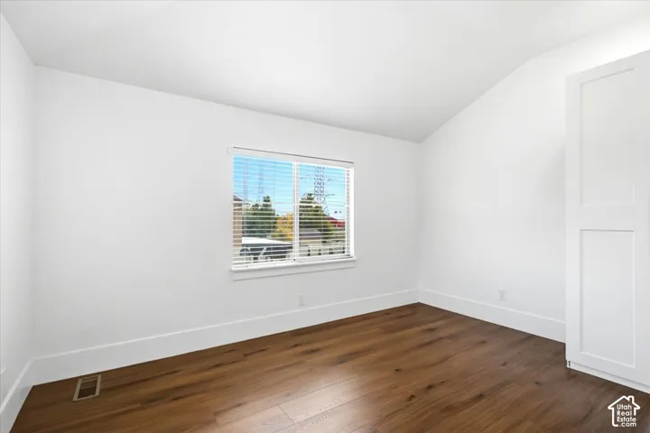 Wood-finish flooring, white walls, built-in white cabinetry, window with blinds, and an angled ceiling