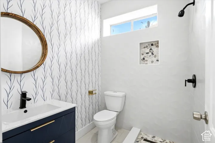 Vanity with a basin sink and matte black faucet, decorative wall covering, textured shower tiling, built-in shower niche with pebble accents, and a transom window