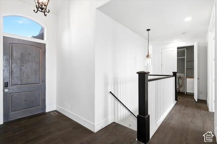 Arched entry door with transom window, dark wood-finish flooring, white walls, black and white staircase railing, and recessed lighting